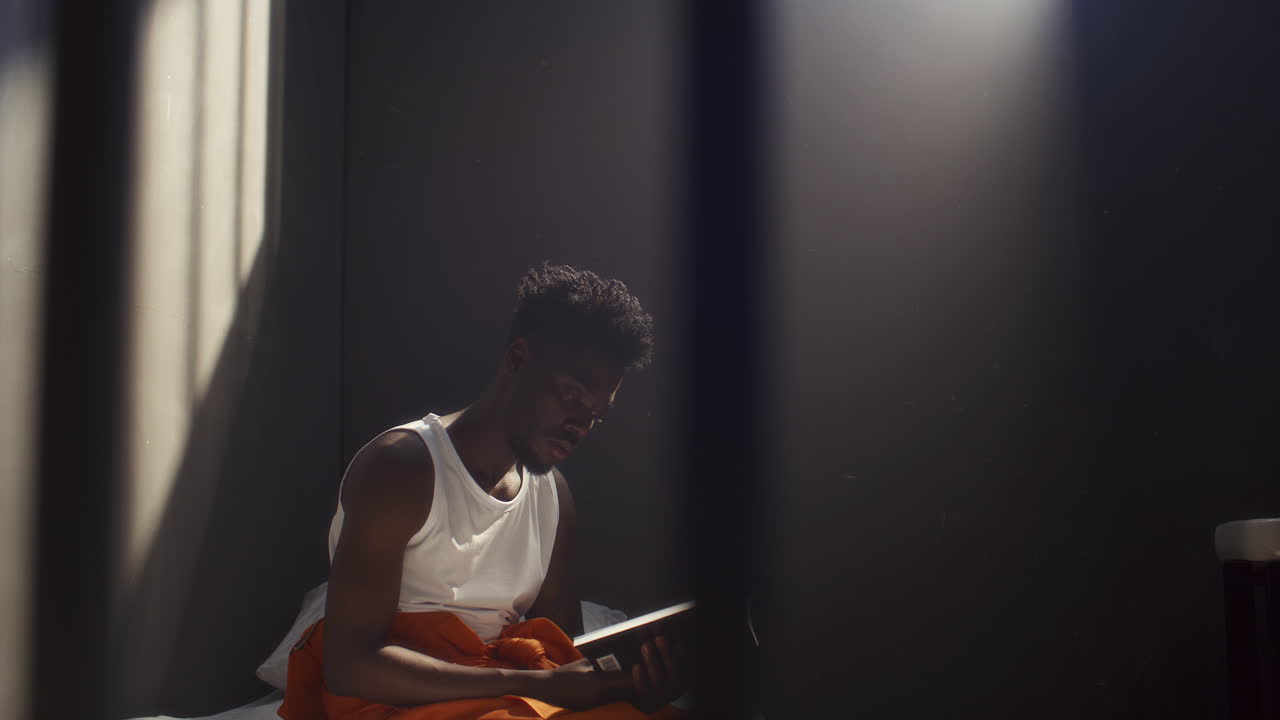 Black Inmate Reading Book while Sitting on Prison Bed
