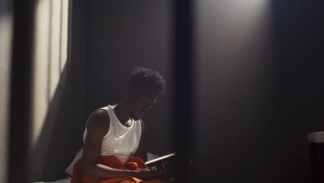 black inmate reading book while sitting on prison bed