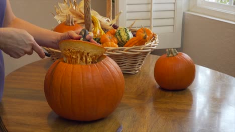 static shot of a woman removing the top of a pumpkin on a dining table with natural light from the side