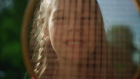 Smiling-girl-looking-camera-through-racket-net-closeup.-Pretty-kid-pose-sunlight