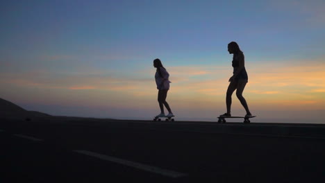 in slow motion, two friends wearing shorts skateboard along a road at sunset, with mountains and a captivating sky as the backdrop