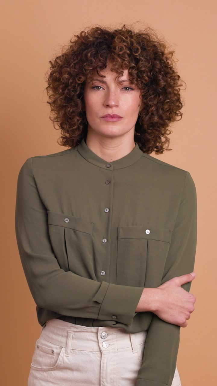 Standing charming young woman with curly hair in beige background. Vertical orientation