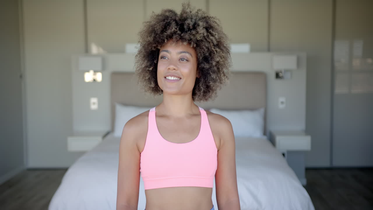 Mulher sorrindo de top esportivo em pé no quarto, pronta para o treino