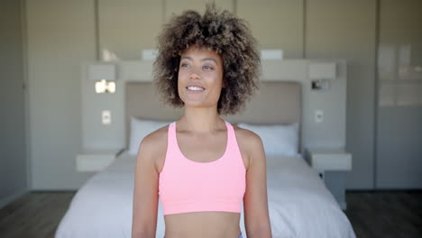 smiling woman in sports bra standing in bedroom, ready for workout