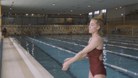 bella joven estira los brazos y los hombros y se concentra antes de nadar en la piscina cubierta