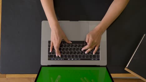 computadora portátil de vista superior está en la mesa con pantalla verde. llave de croma. mujer india caucásica tocando y escribiendo en el teclado. mujer freelance trabajando en casa en línea. trabajo de oficina en cuarentena.