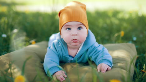 sweet cute baby boy in blue overall lies on brown pillow. healthy kid lies on belly looking up with interest.
