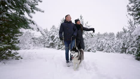 Style-young-couple-having-fun-in-winter-park-near-lake-with-their-friend-husky-dog-on-a-bright-day-hugging-each-other-and-smiling