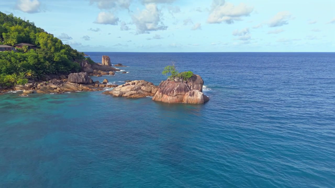 Ripresa cinematografica con drone in pullback inverso che vola all'indietro dal vasto orizzonte oceanico per rivelare splendidi massi di granito e una costa rocciosa ad Anse Soleil, Mahe. Seychelles.