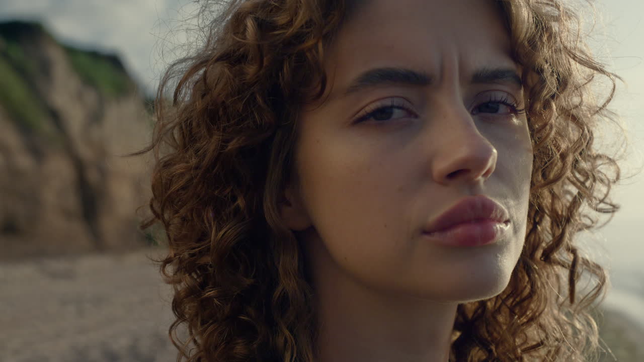 해변에서 해가 뜨는 것을 즐기는 사려 깊은 여자. 꿈꾸는 소녀가 카메라로 머리를 돌리고