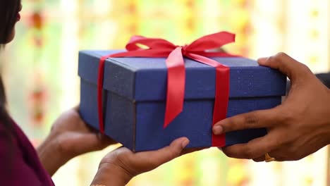 a heartwarming moment of giving as one person hands over a beautifully wrapped gift box with a red ribbon to another against a colorful background