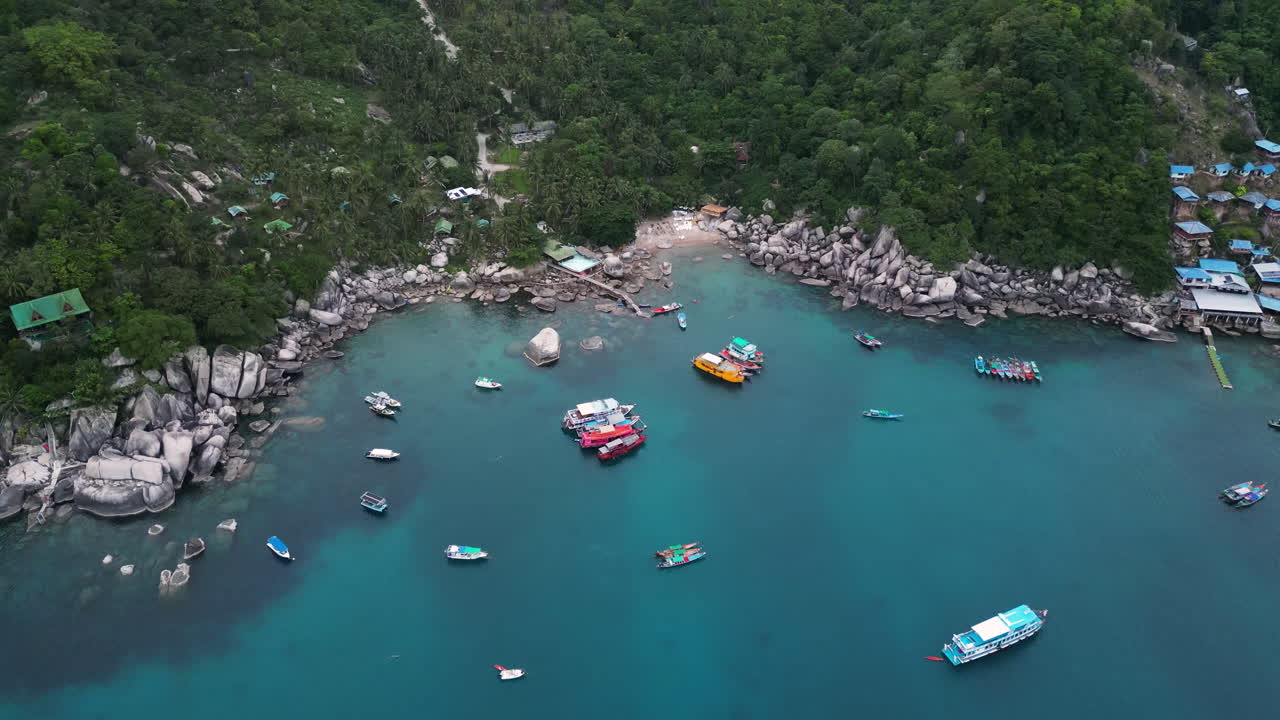 Aerial top down shot of Ao Hin Wong Beach with parking boats on clear water with rocky coastline and jungle on Koh Tao, Thailand
