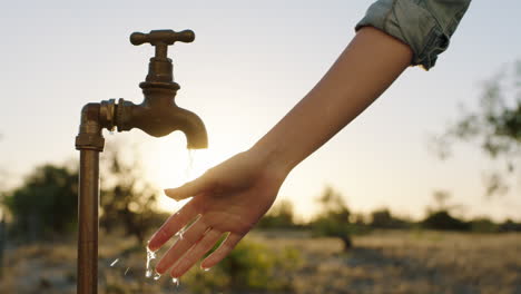 woman washing hand under tap with fresh water on rural farmland at sunrise