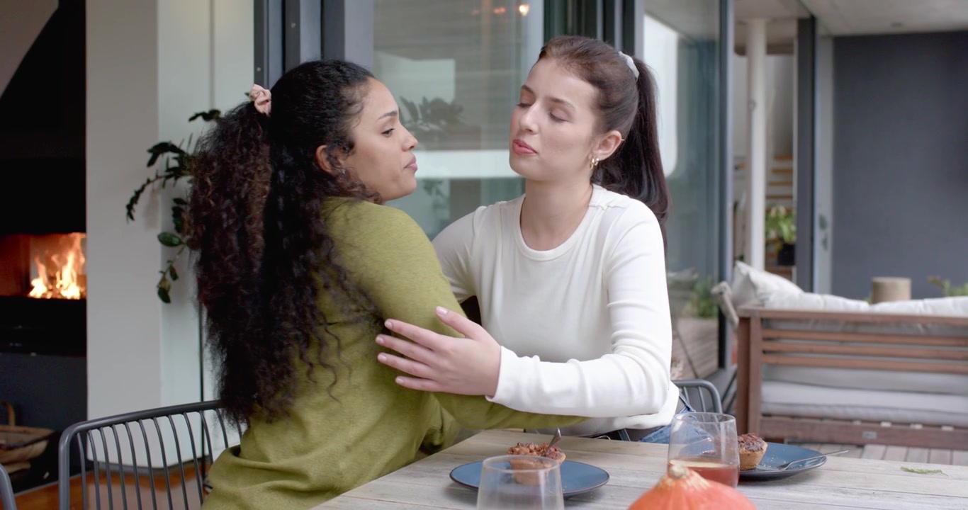Amiche diverse che si abbracciano e si consolano dopo aver condiviso una preoccupazione in un patio coperto con pasticcini