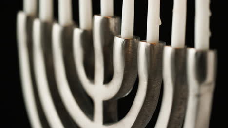 close up, tight crop of silver menorah with white candles on a black background, rack shot