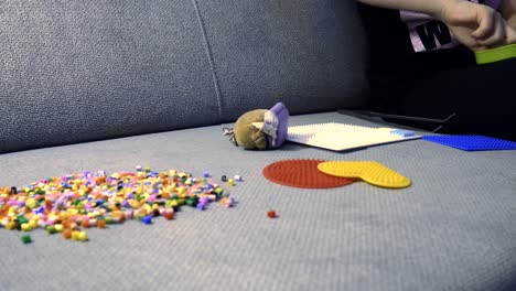 child making art with perler beads,on the sofa