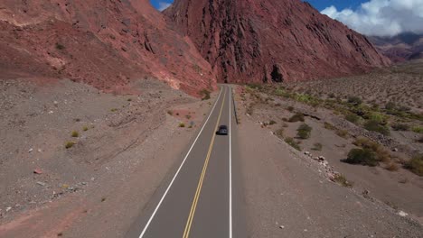 Drone-shot-following-a-grey-car-driving-through-the-Quebrada-Las-Angosturas-in-Catamarca,-Argentina