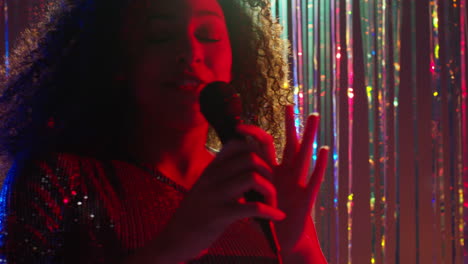 young woman with microphone singing at karaoke nightclub bar or disco with sparkling lights in background 1