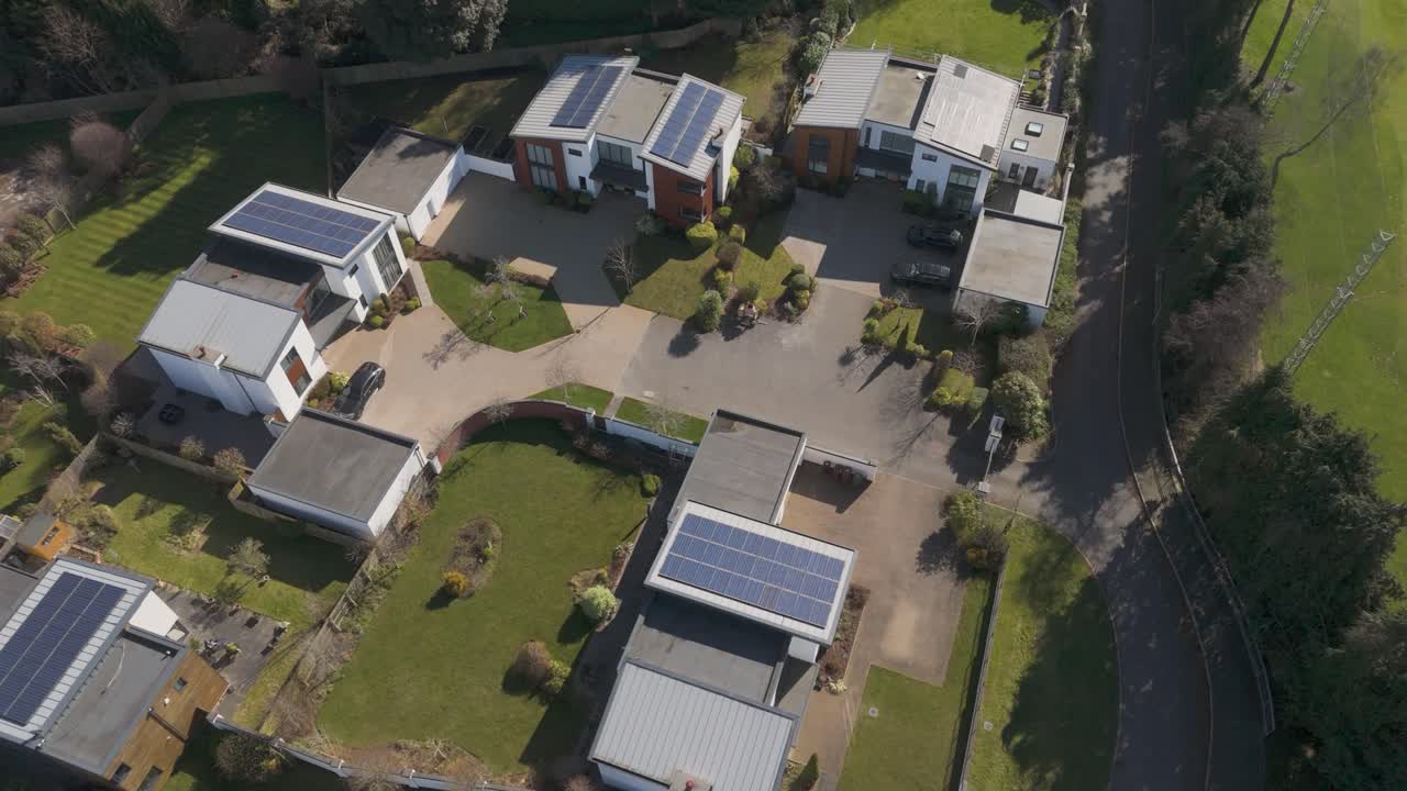 Aerial view of quiet cul-de-sac of angular white houses, rooftop solar panels, hedged lawns and open green buffers illustrating intimate high-spec green living