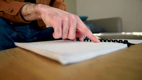 el primer plano de un ciego irreconocible leyendo un libro en braille mientras se sienta en el sofá de casa