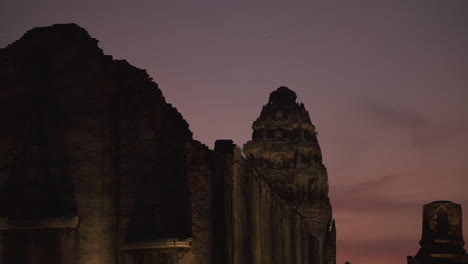 slow motion clip of a bird flying around ancient khmer temple ruins in the city of lopburi in thailand after sunset with a very dramatic purple sky as backdrop