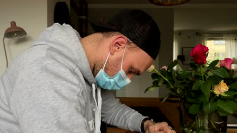 sad caucasian man with protection mask mourning and grieving in front of roses after death of grandmother