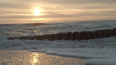 slow motion shot of the waves breaking on the groynes on sylt with the sunset in the background