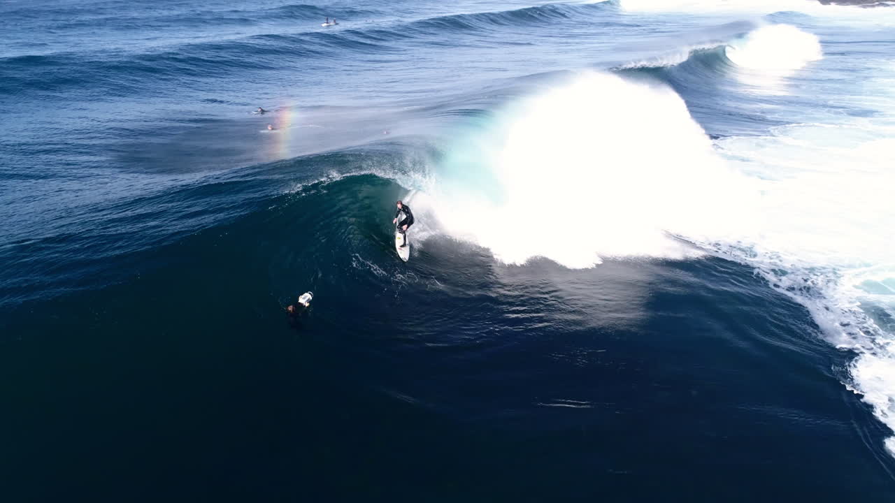 Glassy wave cresting and rolling over reef in bright morning light, dynamic coastal energy, surfer paddles into barrel, aerial tracking and turn backlit