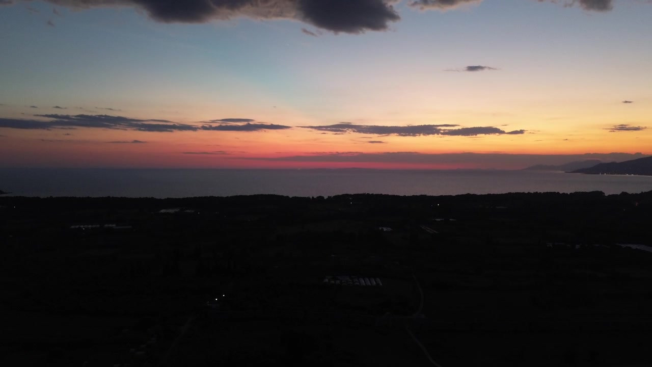 Cinematic drone shot capturing the vibrant orange and pink twilight sky over the calm waters of the Ionian Sea at dusk.