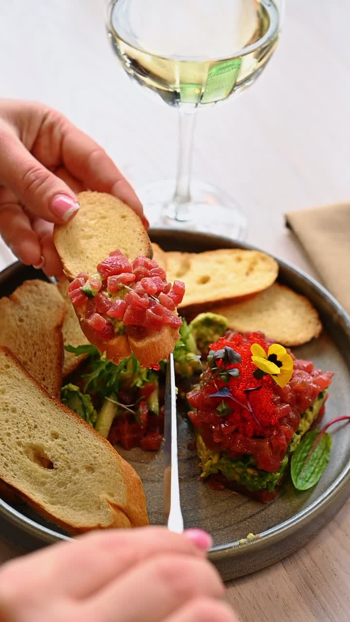 Primo piano di tartare di tonno su fetta di pane. Mano che tiene una fetta di pane tostato guarnita con tartare di tonno e avocado sopra un piatto di ceramica.