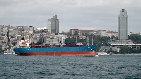 a large cargo ship sails on the water with a city skyline in the background