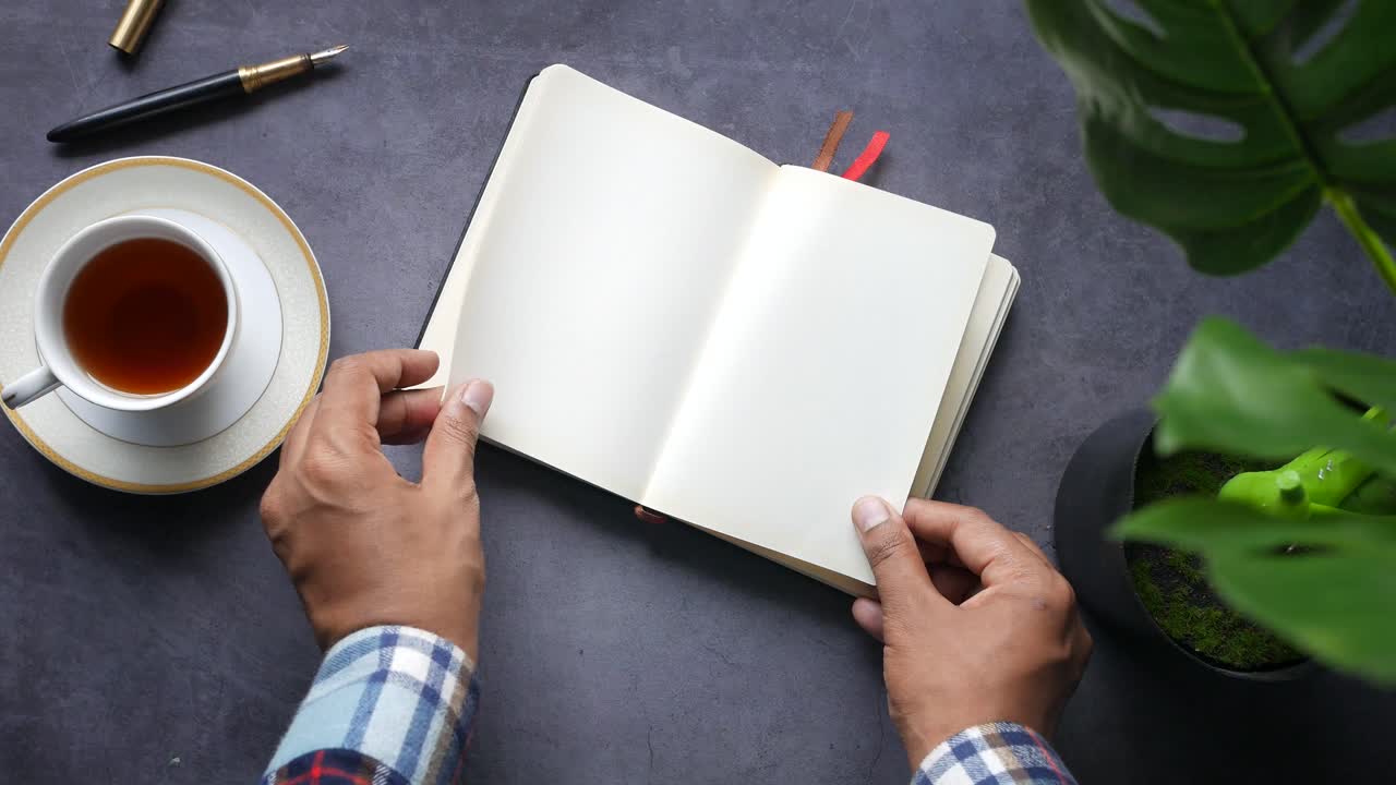 Open notebook on a desk with a cup of tea and a plant