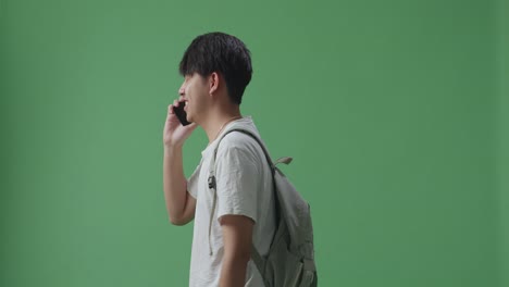 녹색 스크린 스튜디오에서 는 동안 휴대전화로 대화하는 아시아 남성 학생의 측면 시각