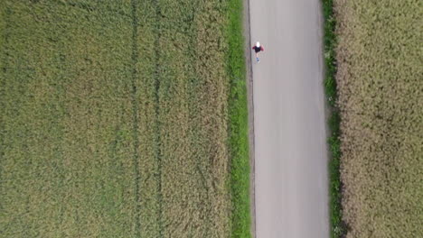 Sporty-Adult-Man-Running-on-Asphalt-Country-Road-by-Crop-Field,-Morning-Cardio-Exercise,-Healthy-Lifestyle---Aerial-Top-Down-Tracking-Motion