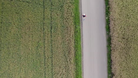 Hombre-Adulto-Deportivo-Corriendo-En-Una-Carretera-Asfaltada-Por-Campo-De-Cultivo,-Ejercicio-Cardiovascular-Matutino,-Estilo-De-Vida-Saludable---Movimiento-De-Seguimiento-Aéreo-De-Arriba-Hacia-Abajo