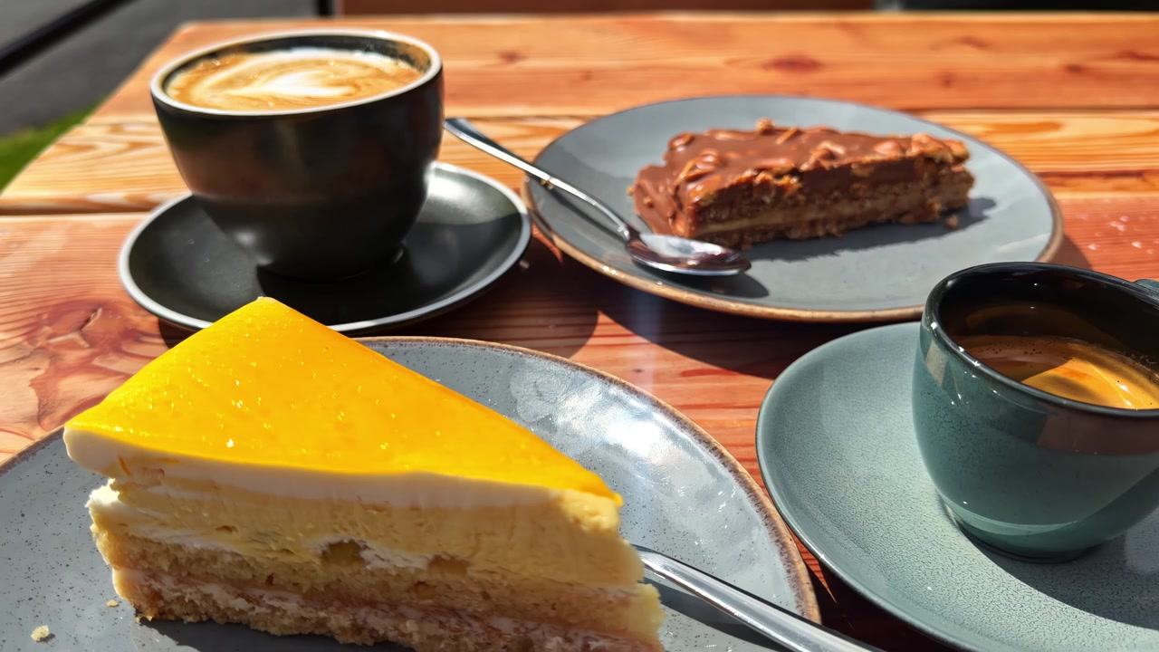 Xícara de café com fatia de torta de chocolate no prato, em ambiente externo.