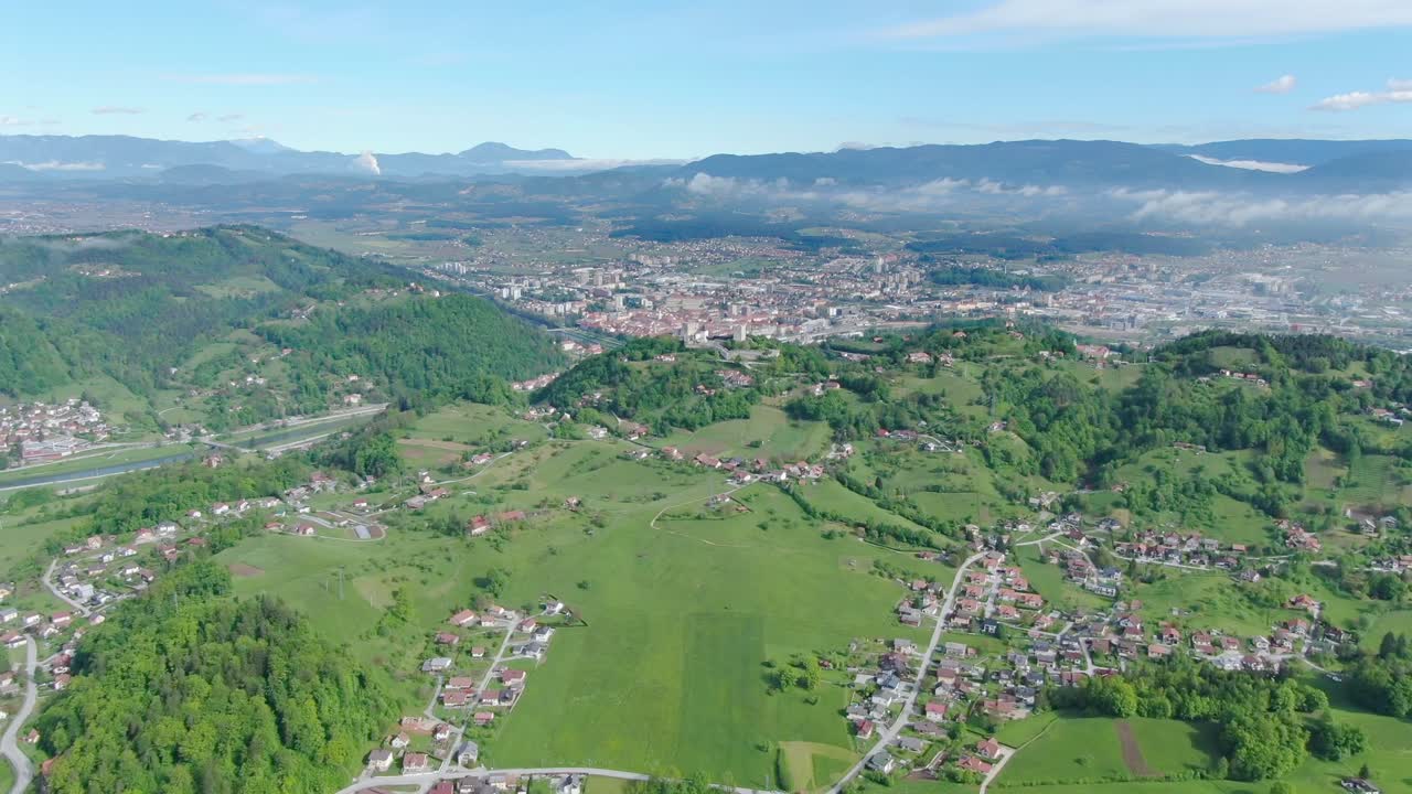 Hilly lush green landscape with small towns in the valley connected by winding roads on a sunny day. Aerial drone shot. Kočevje - Slovenia