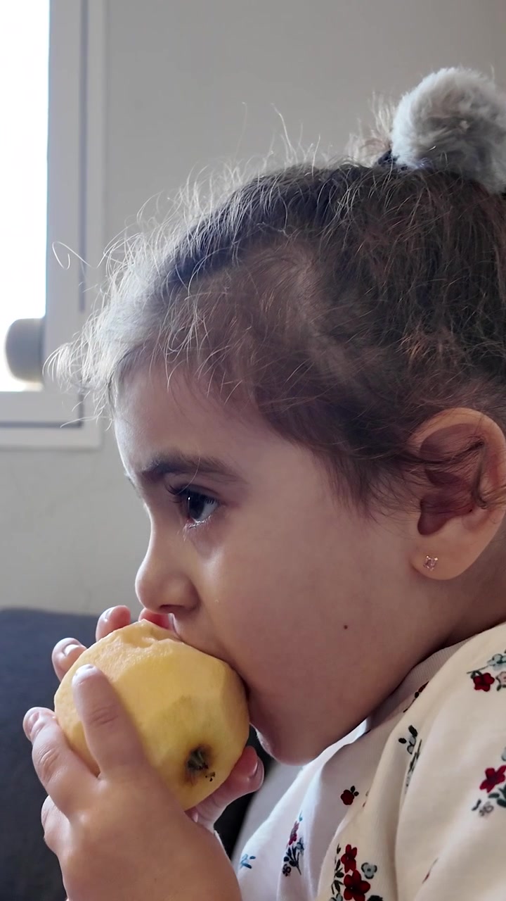 Bambina piccola che mangia una mela sul divano di casa