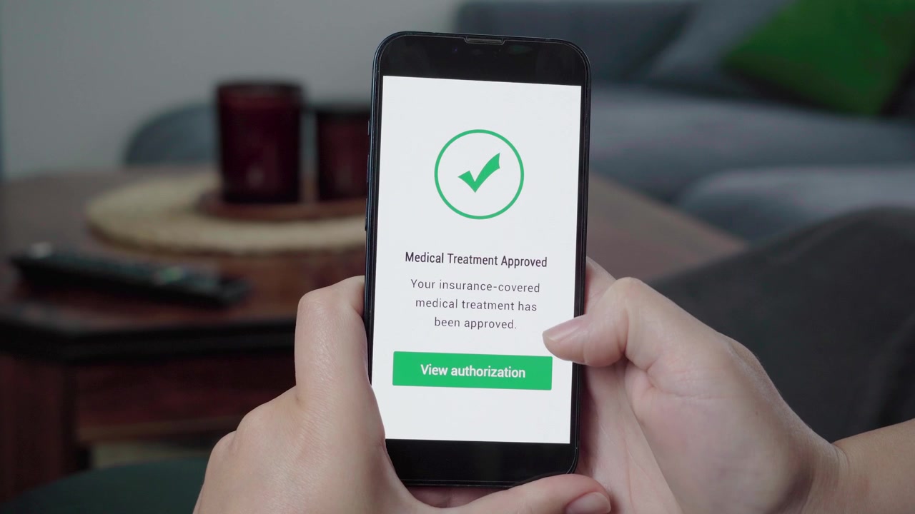 Una persona controlla un'app di assicurazione sanitaria su un telefono e tocca un pulsante di autorizzazione approvata per un trattamento medico.