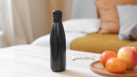 woman places black water bottle on table next to fruits, start of the day