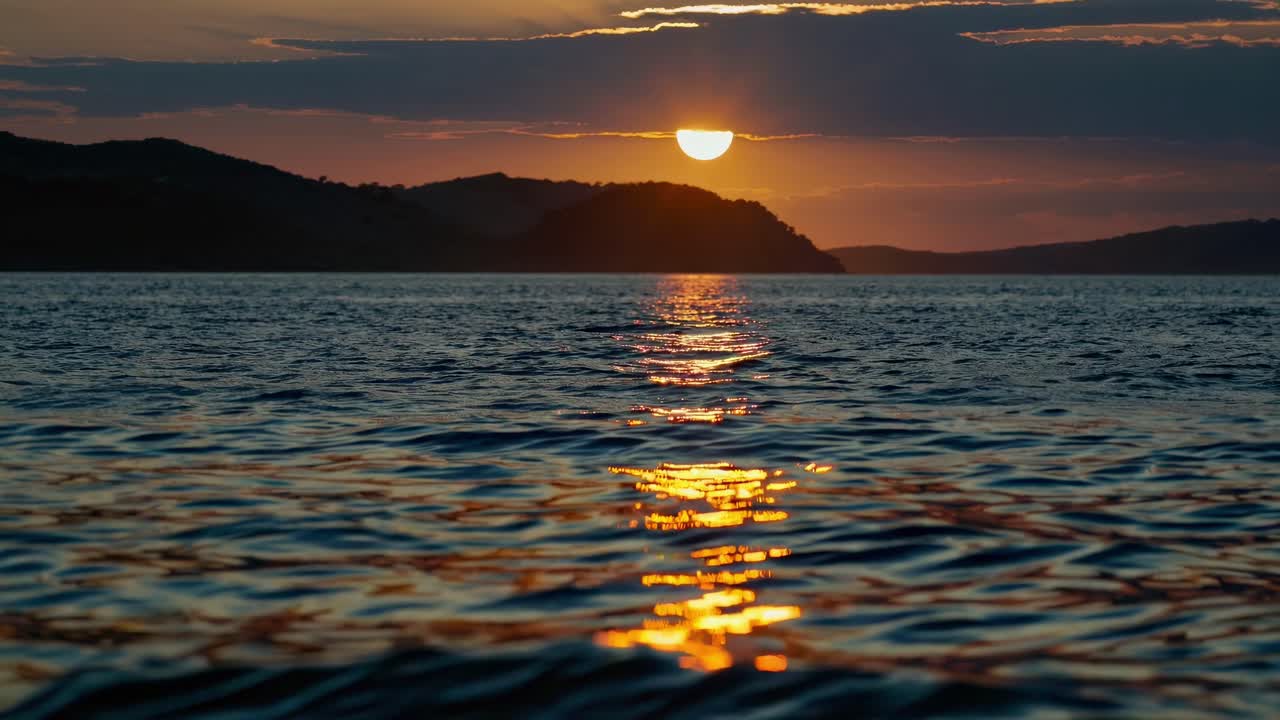 A serene sunset video captures the sun dipping behind hills, reflecting on rippling water