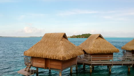 truck right, aerial view of overwater bungalows in bora bora, slowly reveal a island in the background, french polynesia