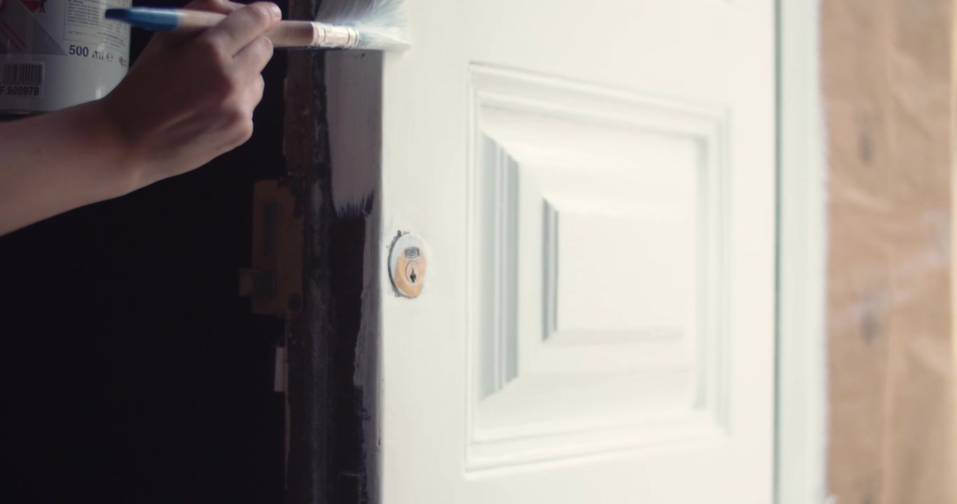 Close up view of a young girl painting white an old wooden doorway