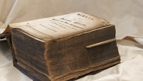 Very-old-thick-bible-with-worn-and-dirty-pages-rests-on-table