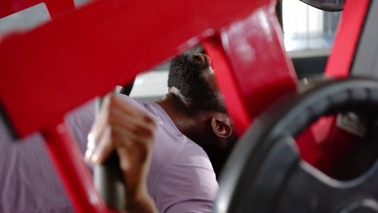 Lifting weights on bench press, african american man focusing on strength training in gym