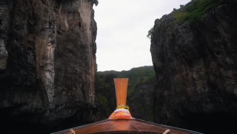 beautifully steep mountain cliffs of wang long bay as a traditional thai boat sails in on a cloudy day in thailand