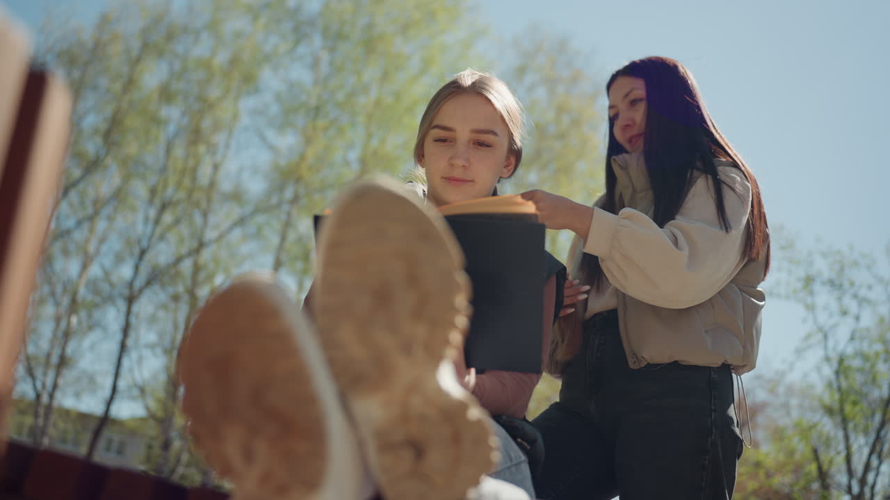 Совместное рецензирование рукописи в спокойной весенней обстановке: азиатский редактор и белый автор обсуждают рукопись в тени деревьев в мягком весеннем солнечном свете.