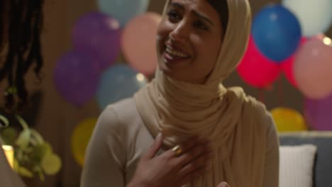 woman giving female friend birthday present at home with party balloons in background 2