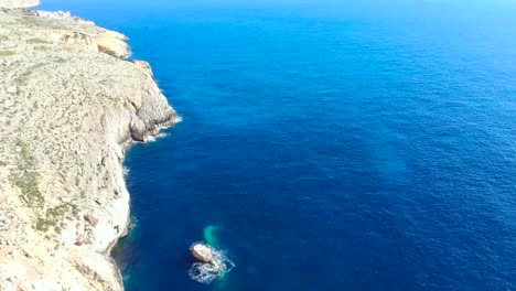 drone shot over rocks and cliffs with wave hitting a small rock in the mediterranean sea of malta 2