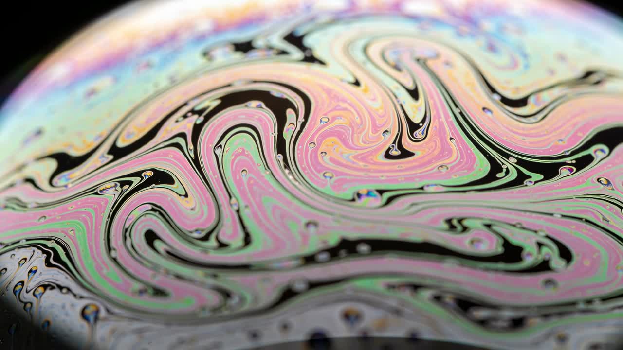 Visualizzazione della superficie di una bolla che si sposta e si assottiglia a causa della tensione in macro in studio, con bande iridescenti.